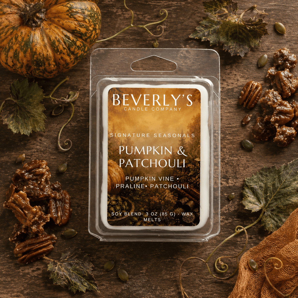 Pumpkin and Patchouli wax melt clamshell surrounded by a whole pumpkin, pecan pralines, autumn leaves, and pumpkin seeds on a dark wood surface